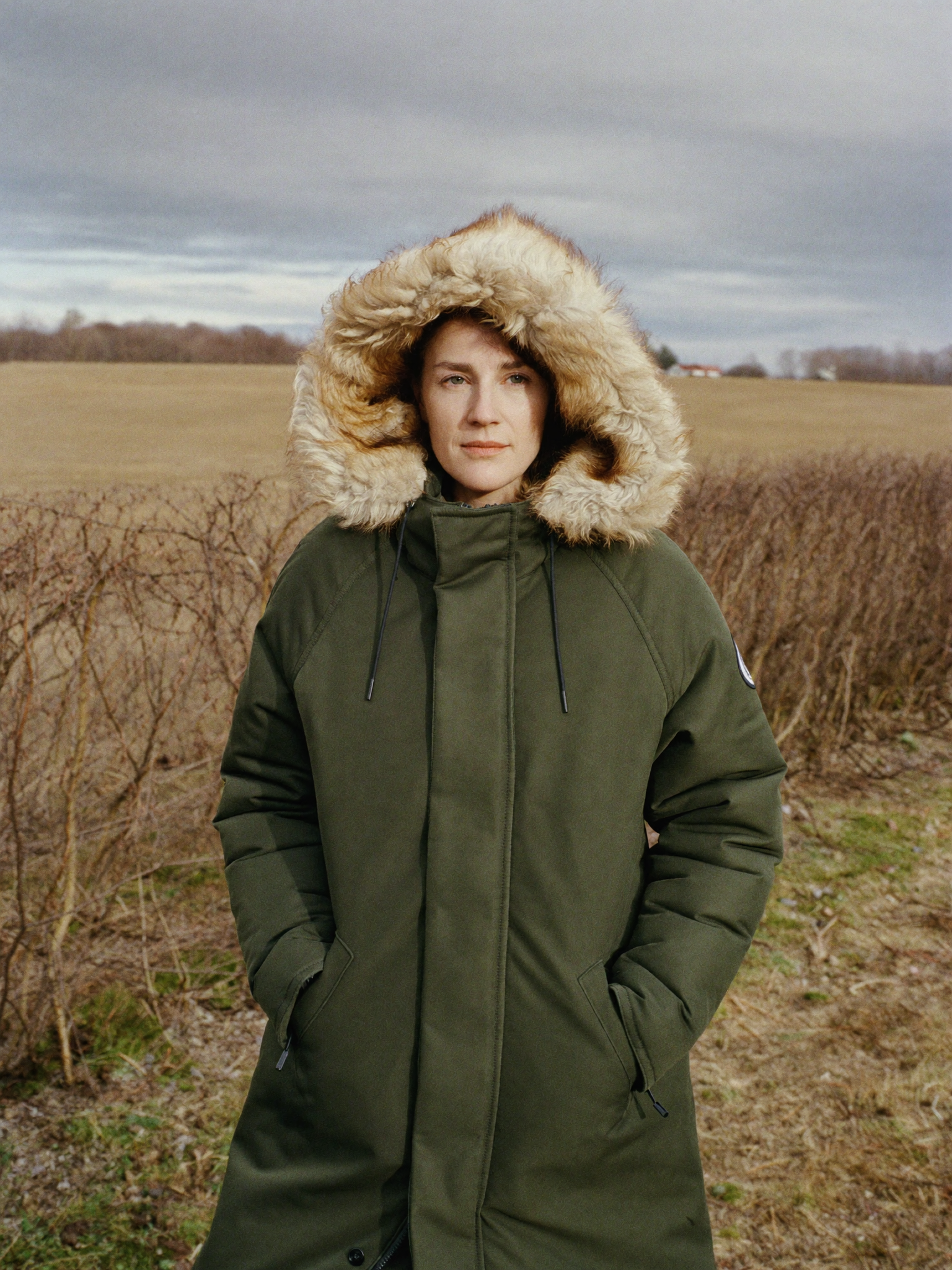 Woman walking a dog in a long olive diamond quilted coat seen from behind