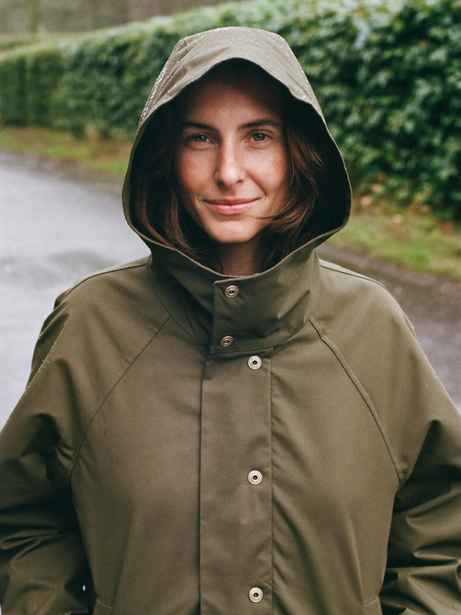 Woman in an olive waxed cotton rain coat with the hood up on a wet country lane