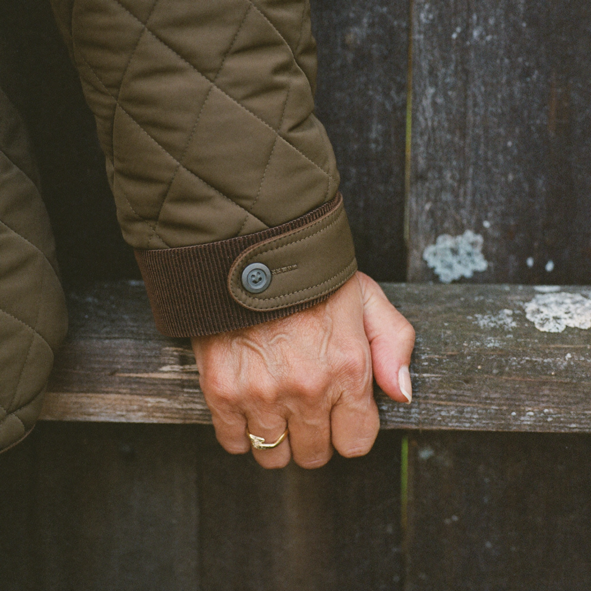 Close detail of a corduroy cuff binding and stud on an olive quilted jacket